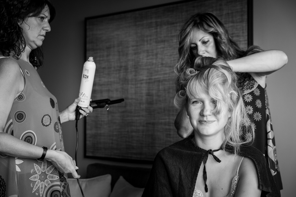 Fotografo Matrimonio Langhe La sposa accenna un sorriso mentre le damigelle conciano i suoi capelli