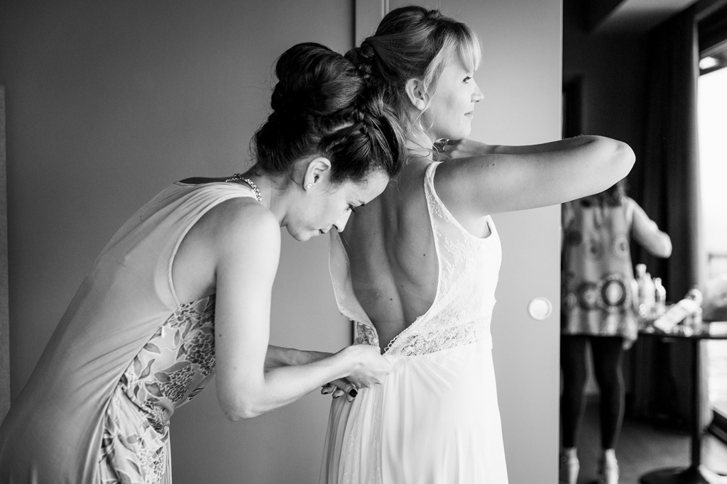 Fotografo Matrimonio Langhe Una damigella aiuta la sposa nel chiudere il vestito