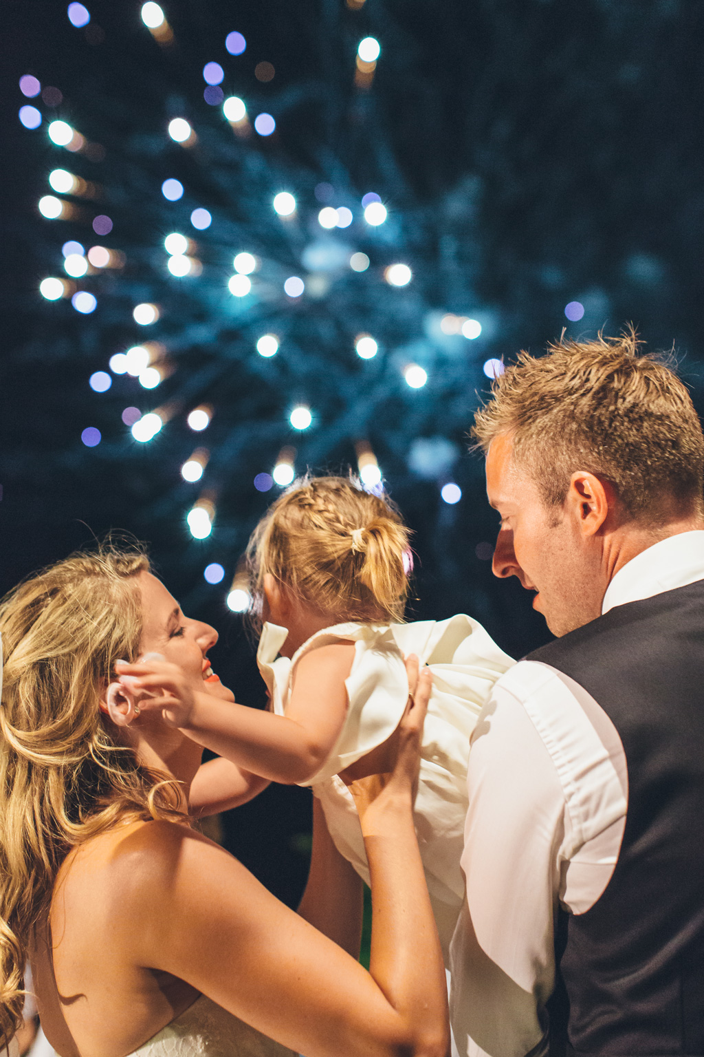 Gli sposi stringono una bambina durante i botti d'artificio