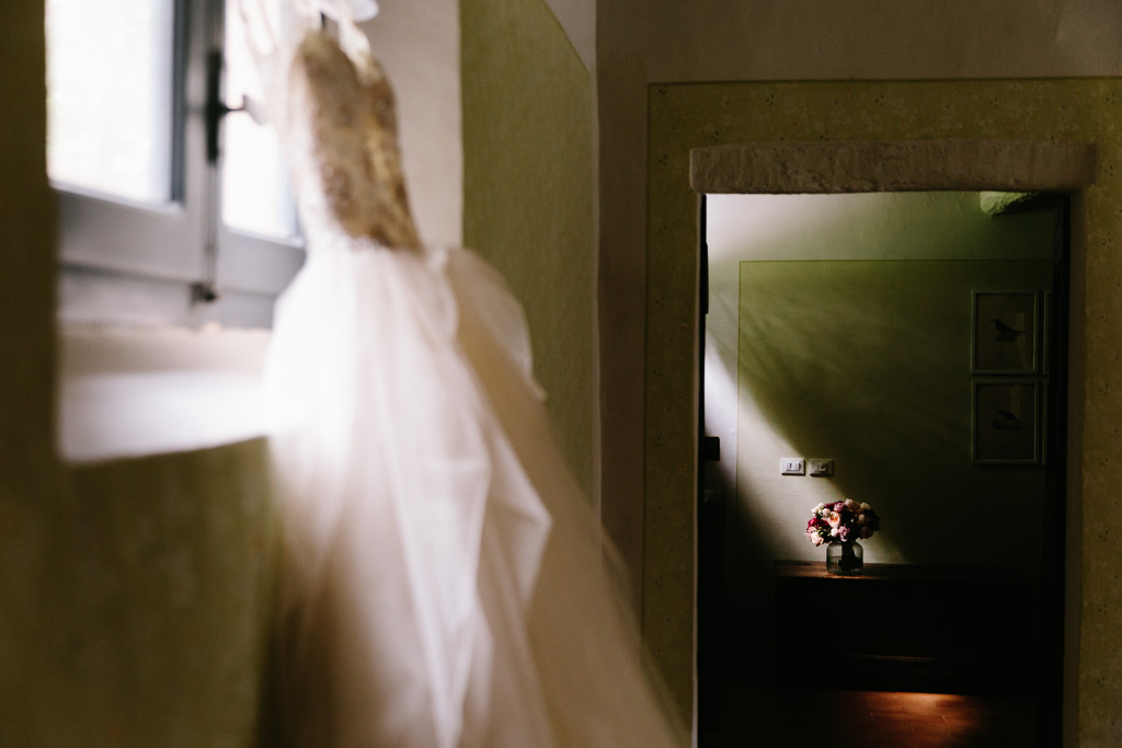 Fotografo Matrimonio Convento Dell'Annunciata Medole Il vestito della sposa appeso alla finestra prende una luce meravigliosa