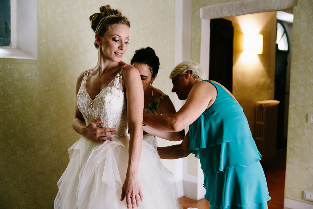 Fotografo Matrimonio Convento Dell'Annunciata Medole La mamma e l'amica allacciano l'abito alla sposa