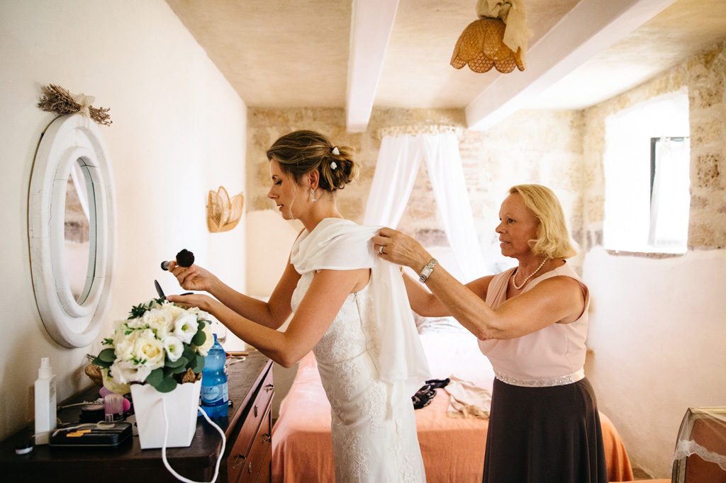Fotografo Matrimonio Basilica San Galgano Toscana La mamma sistema il vestito alla sposa mentre prende dei trucchi