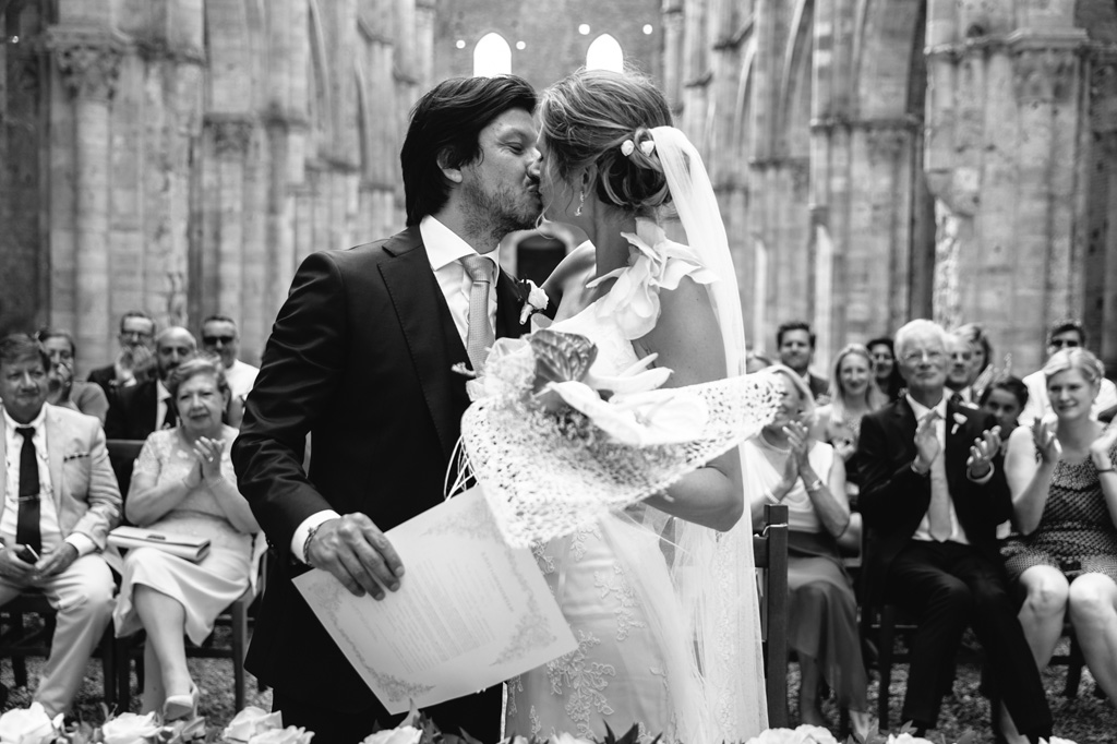 Fotografo Matrimonio Basilica San Galgano Toscana Il bacio degli sposi alla conclusione della cerimonia mentre gli invitati appaludono