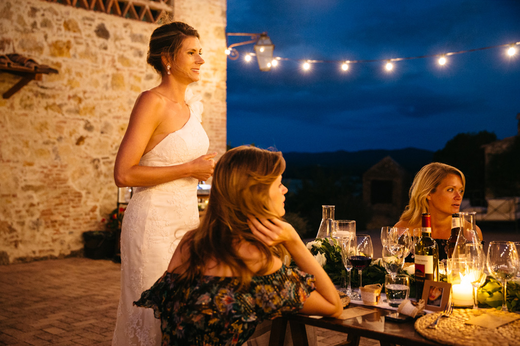 Fotografo Matrimonio Basilica San Galgano Toscana La sposa in piedi davanti al tavolo sorride agli invitati