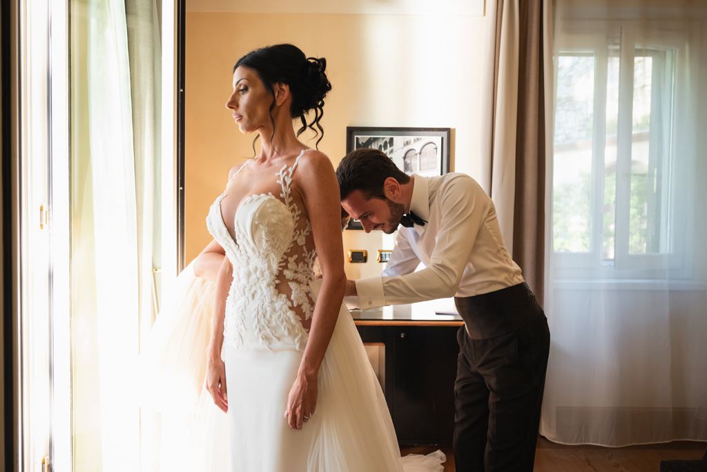 Fotografo Matrimonio Lago di Como Casta Diva Mandarin Lo sposo allaccia il vestito alla sposa